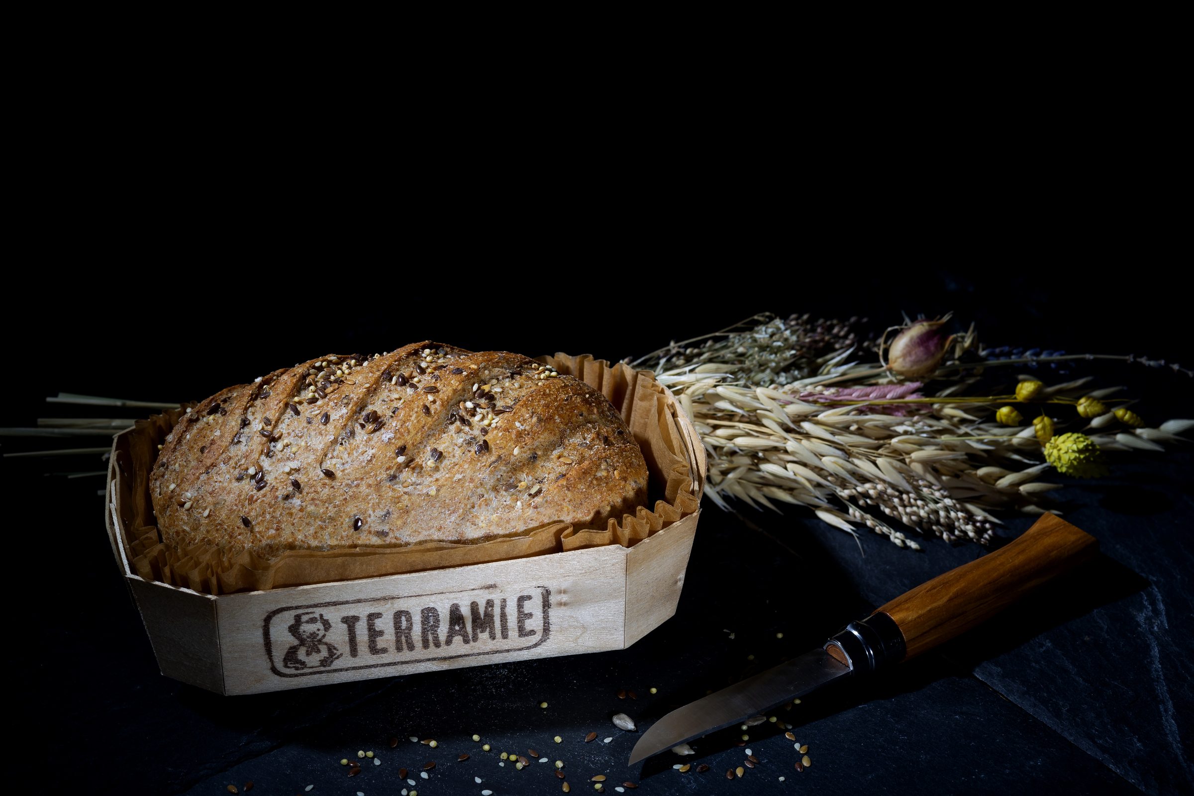 Pain de céréales de la Boulangerie Bretteau sur ardoise, aux côtés d'un bouquet de blé